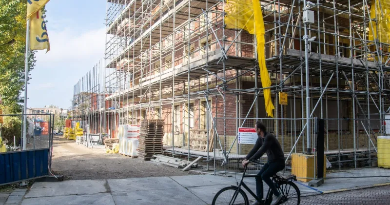 Bouwplaats met een gebouw in aanbouw, fietser fietst voor de bouwplaats langs
